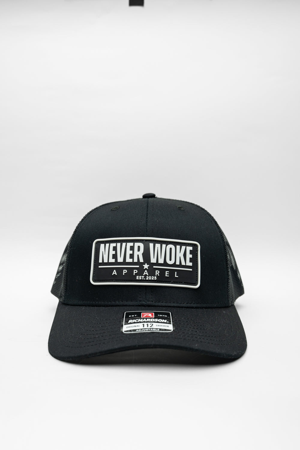 Black cap with 'Never Woke Apparel' logo on a black background with white boarder and letters